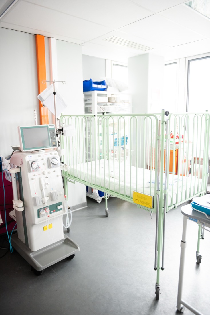 Un lit à barreaux vert et un générateur de dialyse dans une chambre claire.