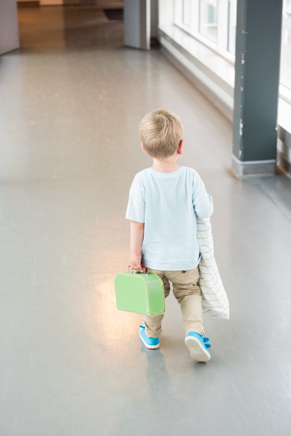 Un jeune enfant s'éloigne dans un couloir lumineux de l'hôpital, une petite valise verte à la main.